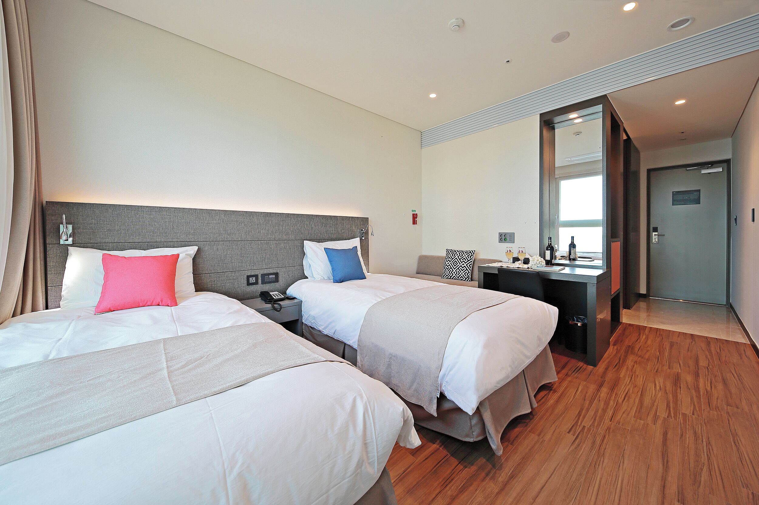 Habitación de hotel con dos camas, un escritorio, un espejo y una puerta.
