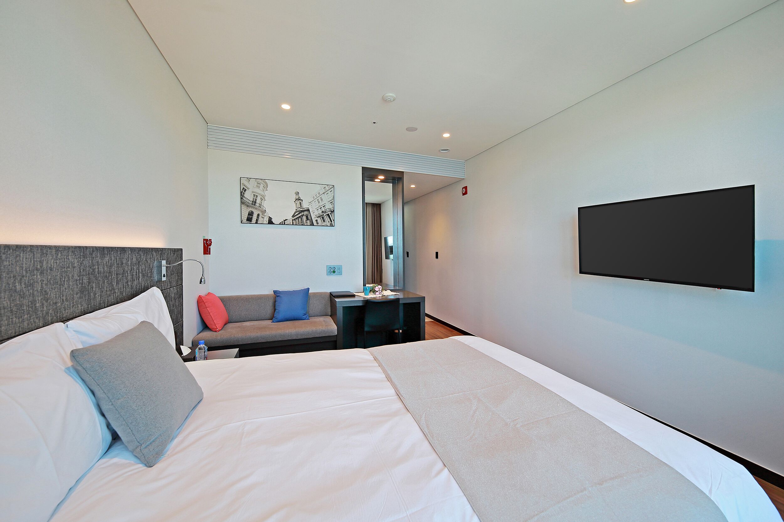 A modern hotel room with a large bed, a flat-screen TV, a sofa, and a desk.