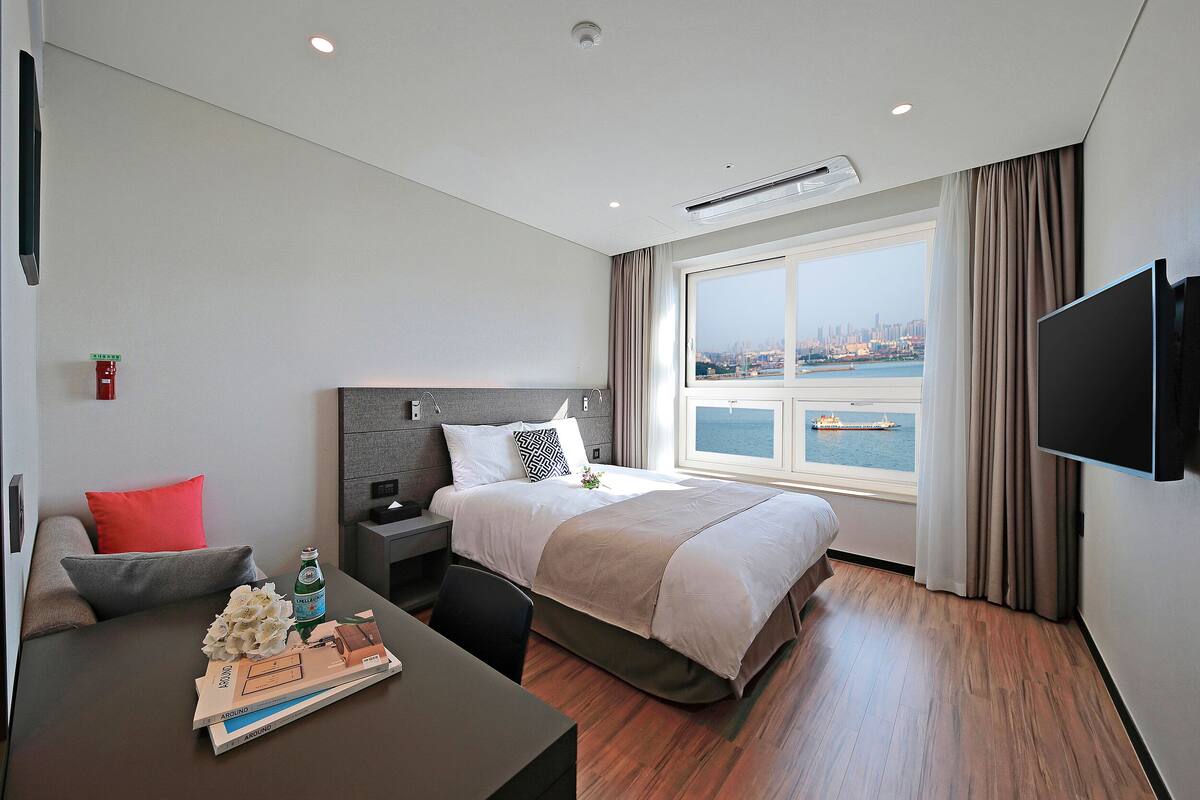 A modern hotel room with a large bed, a desk, and a TV.