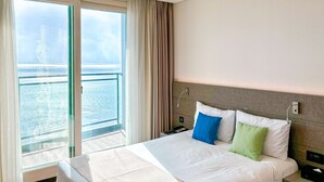 A hotel room with a large bed, a nightstand, a bedside table, and a view of the sea through a large window. - Airsky Hotel (Incheon)