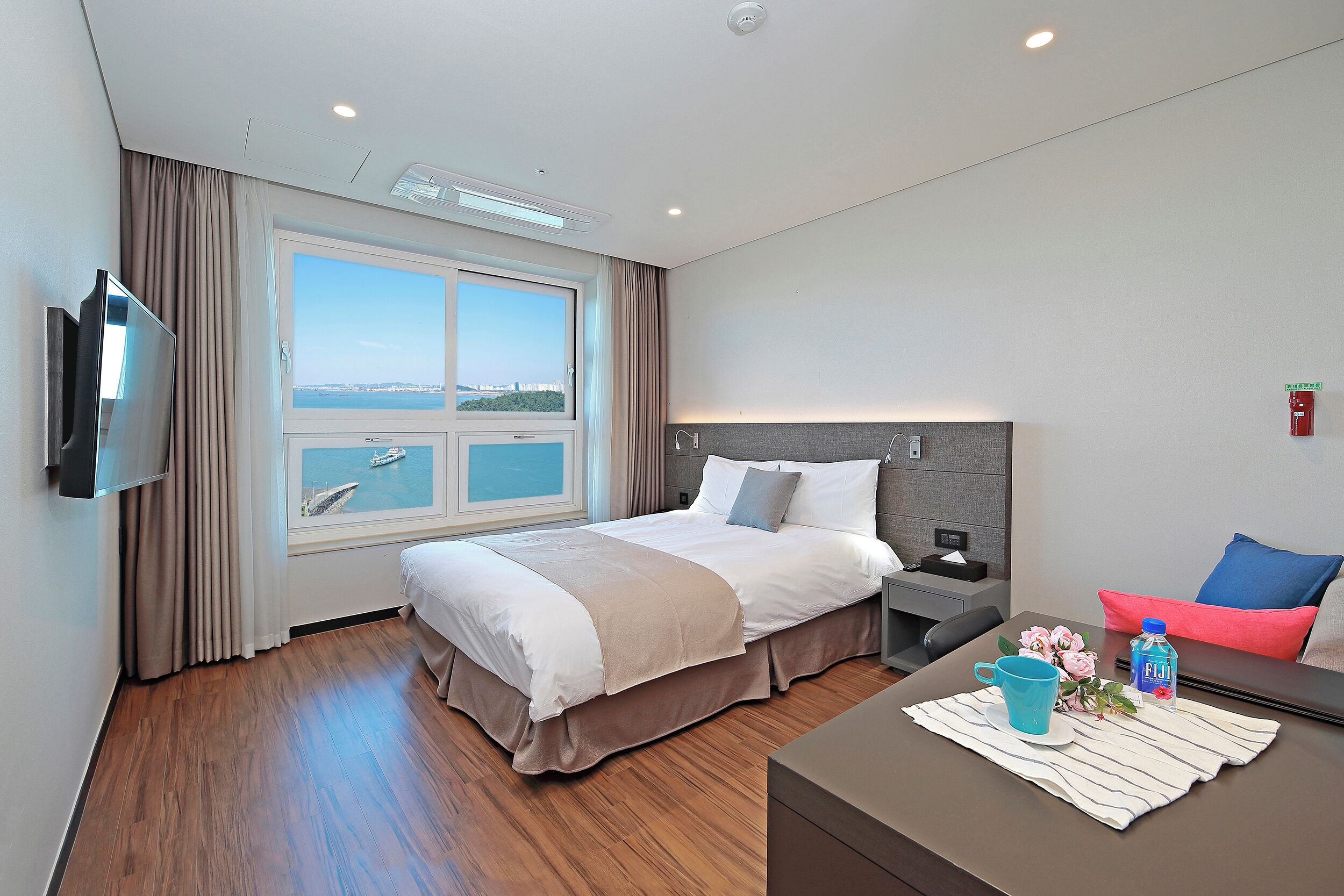 Une chambre d’hôtel moderne dotée d’un grand lit, d’une télévision à écran plat, d’un bureau avec une chaise et d’une fenêtre donnant sur la mer.