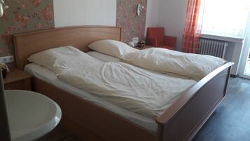 A double bed with white linens, a wooden headboard, a bedside table with a lamp, a small table with a fruit bowl, and a radiator.