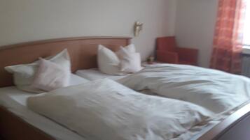 A double bed with white linens and pillows, a wooden headboard, and a nightstand with a lamp.