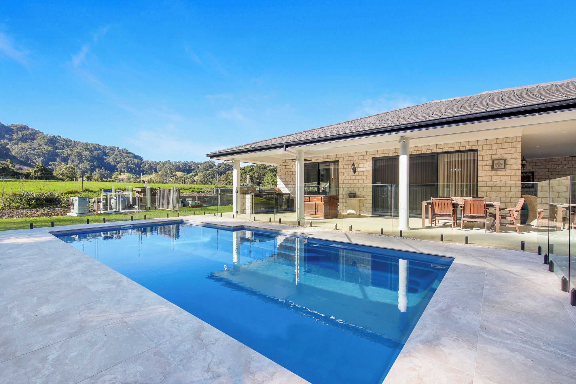 A modern house with a swimming pool, outdoor seating, and a view of the mountains.