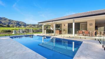 A modern house with a swimming pool, outdoor seating, and a view of the mountains.