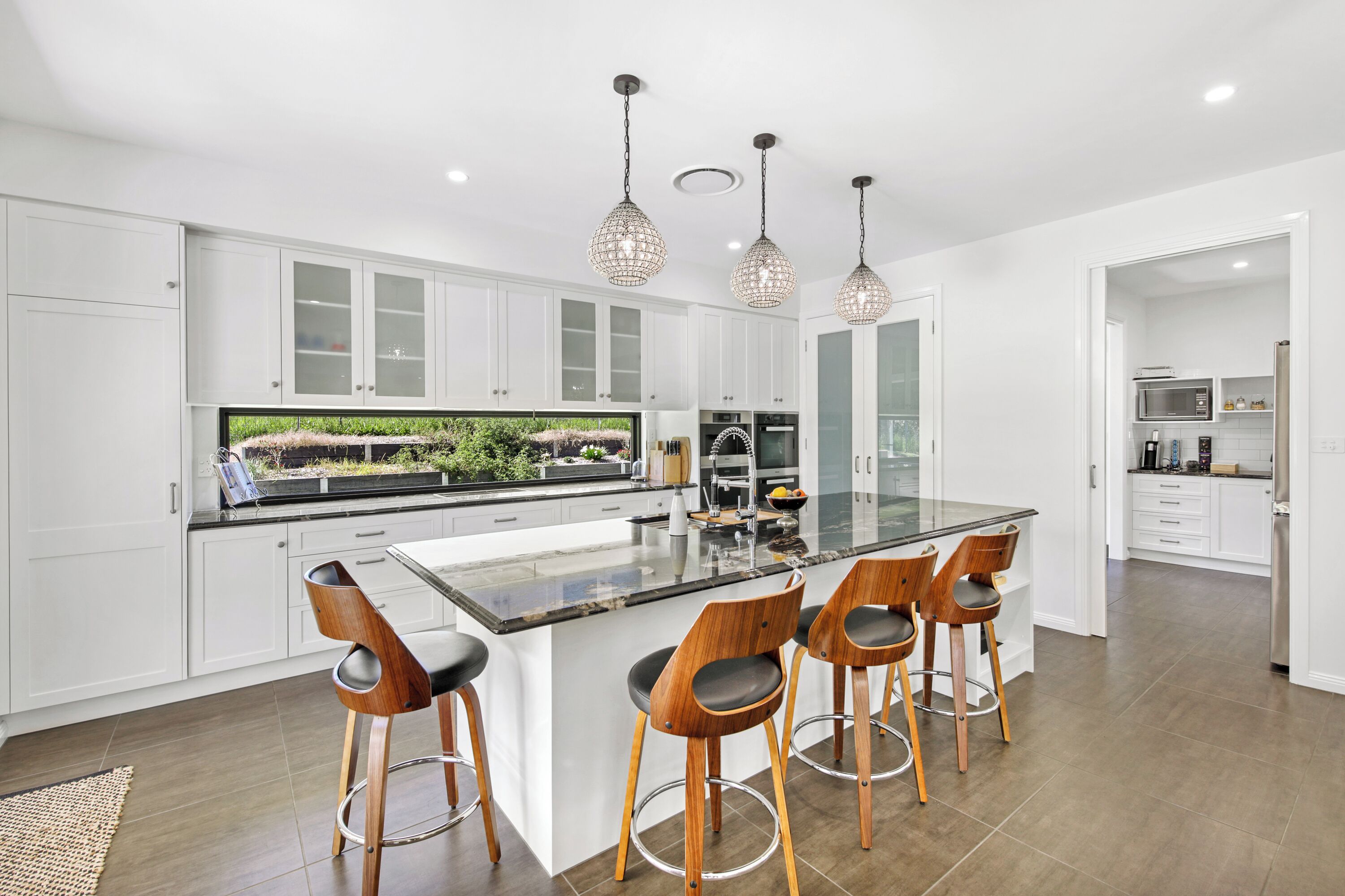 A modern kitchen with white cabinets, a large island with bar stools, and pendant lighting.