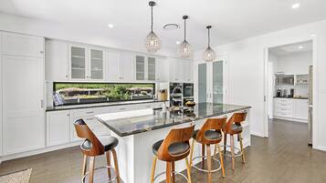 A modern kitchen with white cabinets, a large island with bar stools, and pendant lighting.