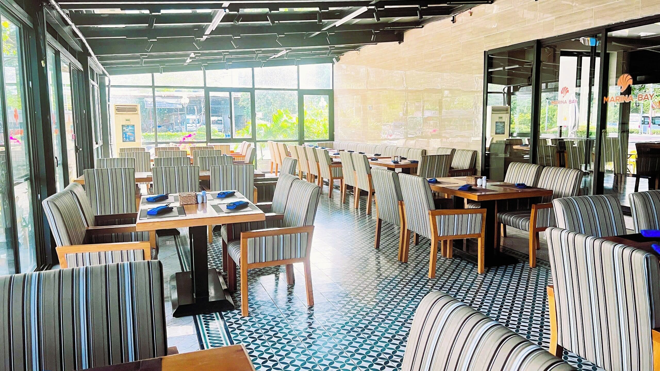 Un restaurante con sillas y mesas a rayas, ventanas amplias y suelo de baldosas.