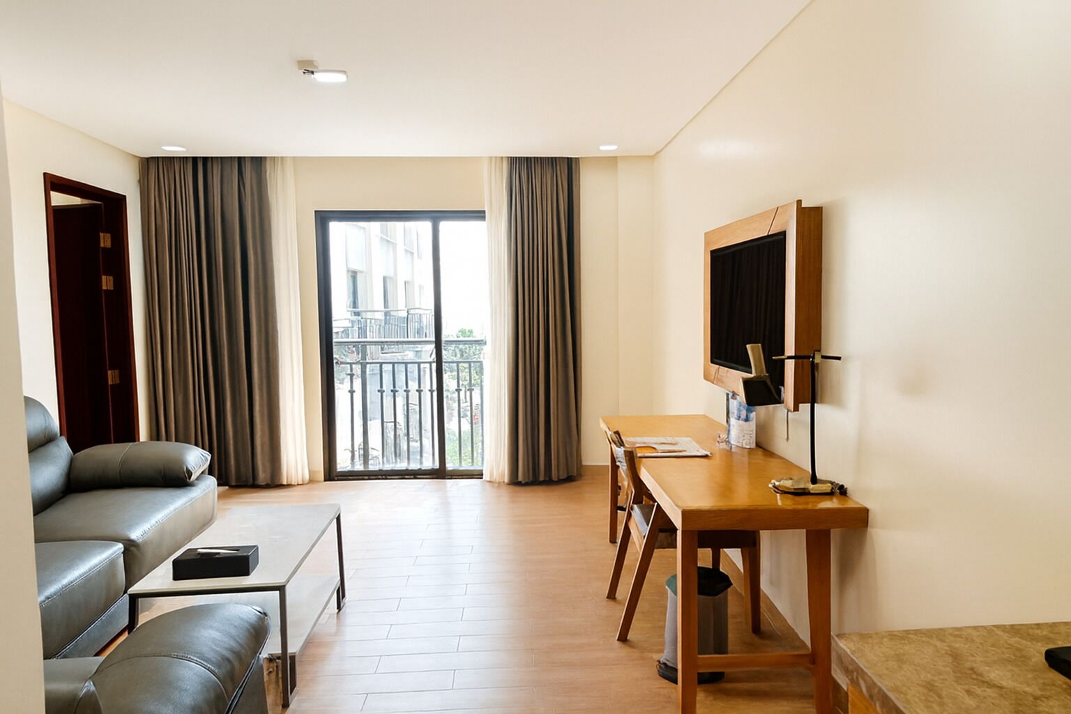 Habitación de hotel moderna con sofá, un escritorio de madera, televisor y balcón con cortinas.