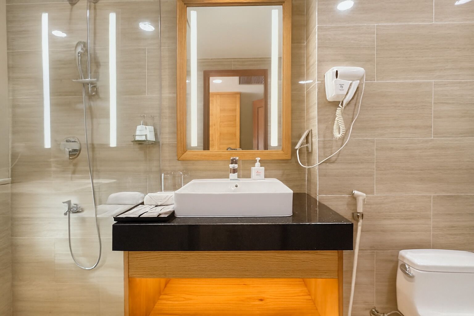 A modern bathroom with a black countertop sink, a mirror, a handheld showerhead, and a toilet.