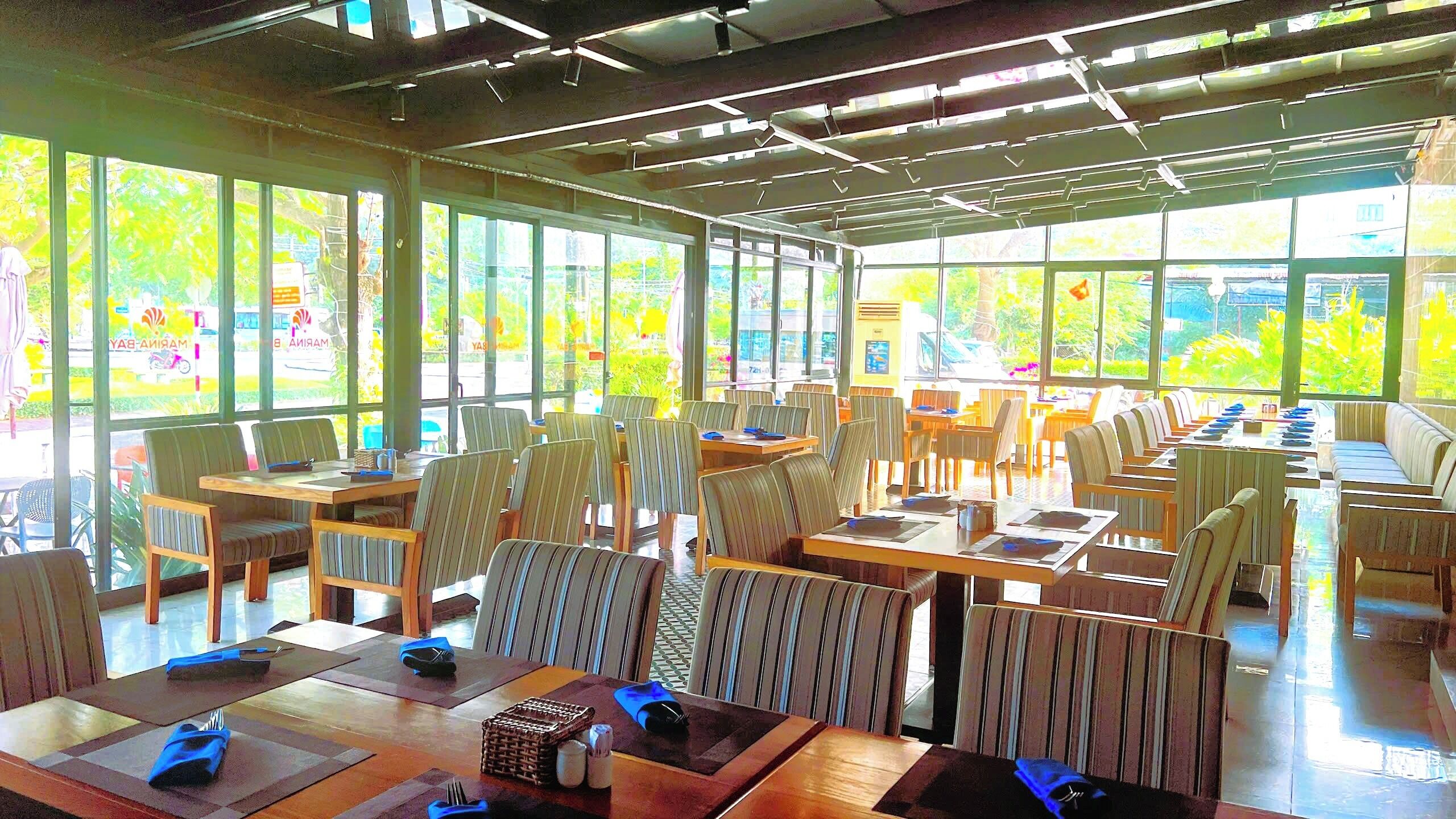 Un ampli restaurant amb grans finestres, taules de fusta i cadires a ratlles.
