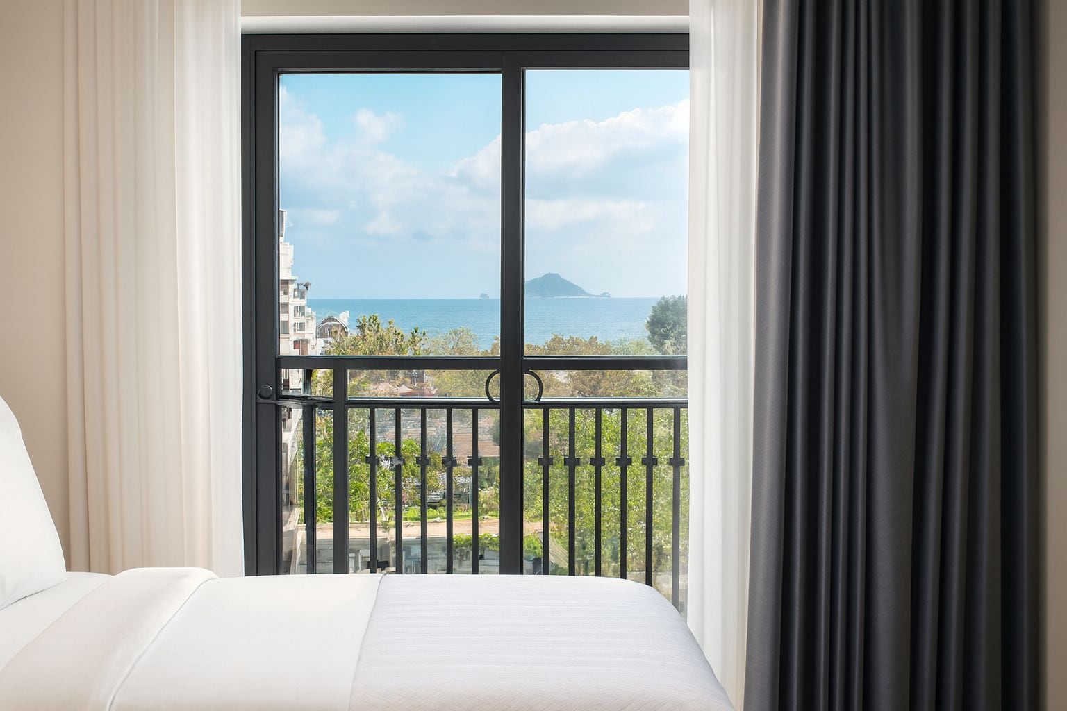 Habitación de hotel con cama, vista al mar y balcón con barandilla.