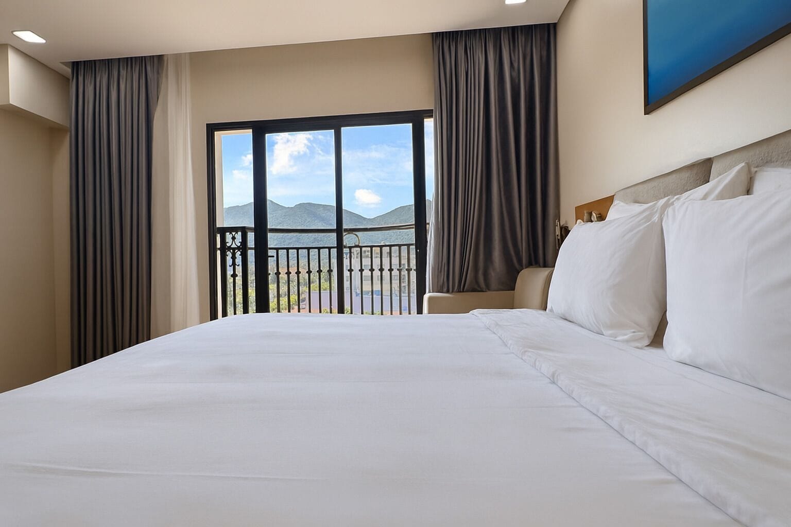 A hotel room with a large bed, a view of mountains through a sliding door, and a balcony with a railing.