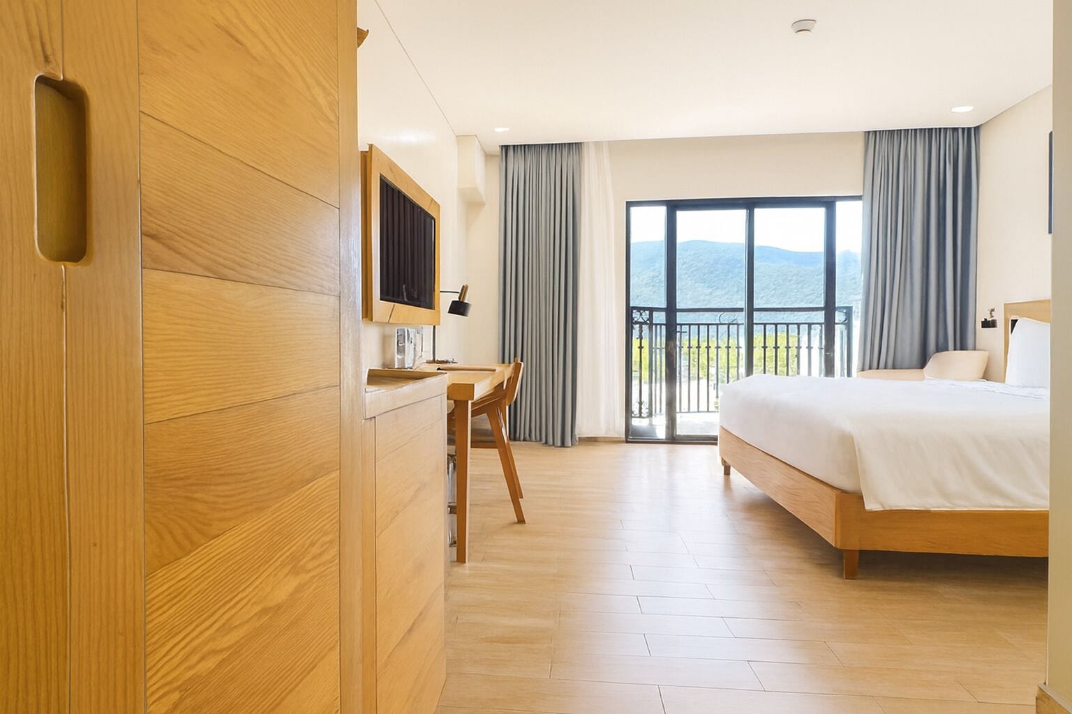 Habitación de hotel con un escritorio de madera, una cama y un balcón con vistas.
