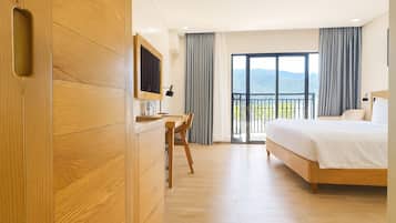 Habitación de hotel con un escritorio de madera, una cama y un balcón con vistas.