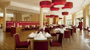 A spacious dining area with multiple tables and chairs, large red pendant lights, and a large window providing natural light. - Millenium Hotel Ramallah (Ramallah)