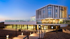 A modern hotel with a glass facade, outdoor seating, and a pool area.