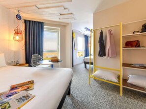 A hotel room with a bed, a small table, a chair, a hanging light, a wardrobe, and a window with curtains. - Ibis Styles La Rochelle Thalasso Chatelaillon (Chatelaillon-Plage)