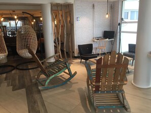 A modern interior with unique wooden rocking chairs, a white brick wall, and a view of the city. - Ibis Styles La Rochelle Thalasso Chatelaillon (Chatelaillon-Plage)