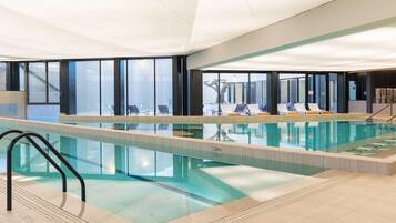 Una piscina interior con agua cristalina, un trampolín y sillones de descanso.