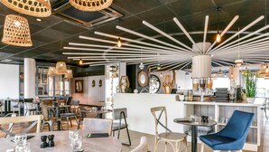 A modern restaurant interior with round tables, chairs, hanging wicker lamps, and a central light fixture.