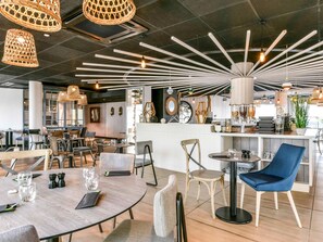 Ein modernes Restaurant-Interieur mit runden Tischen, Stühlen, hängenden Korbtaschenlampen und einer zentralen Leuchte.