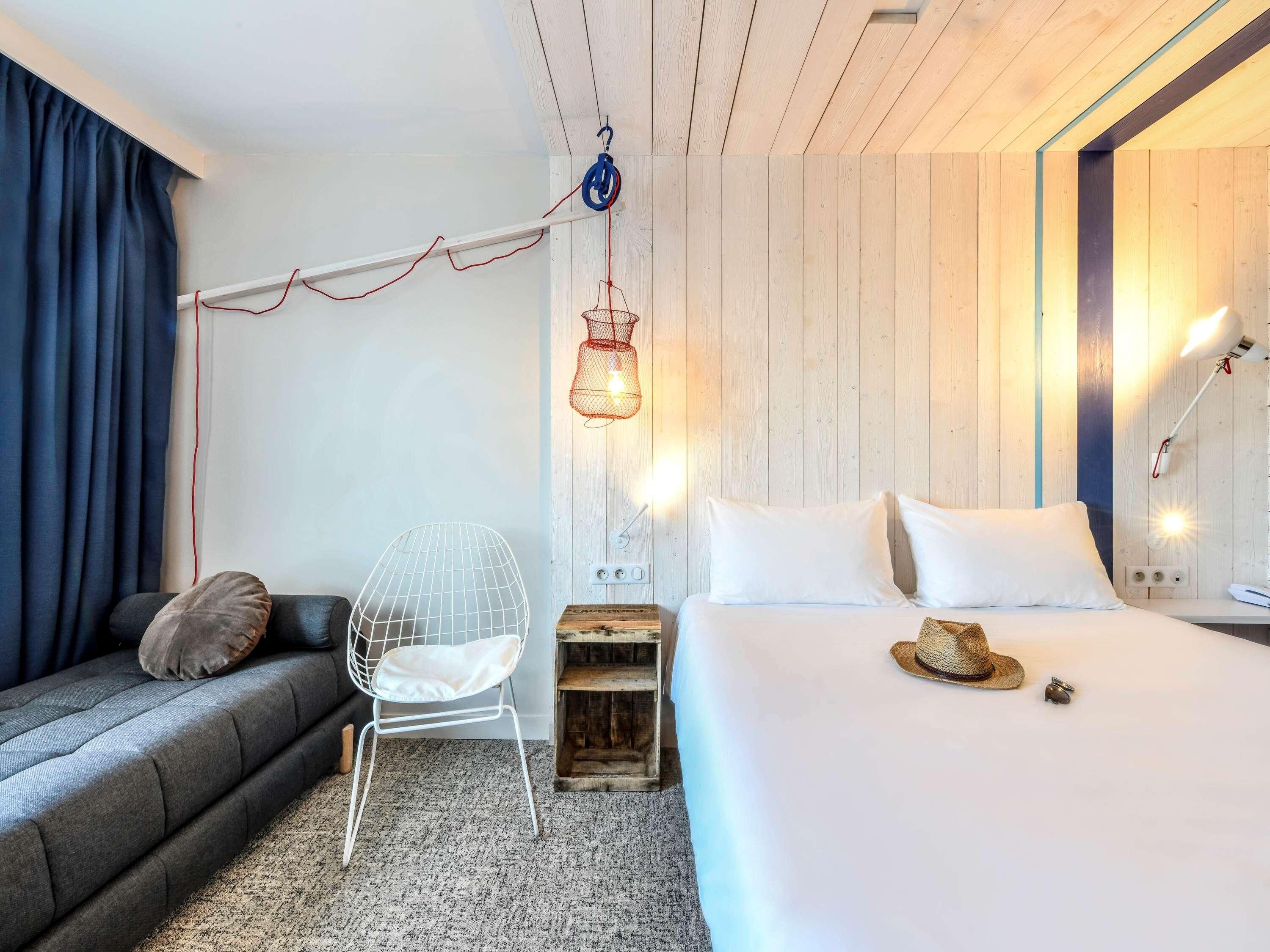 Habitació d'hotel moderna amb un llit, una cadira, un penjallum i un panell de capçal de fusta.