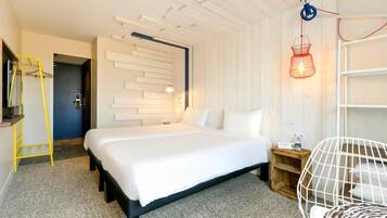 A hotel room with a bed, a desk, a chair, a ladder, and a wall-mounted shelf.