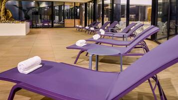 Ein moderner Innenbereich zur Entspannung mit violetten Lounge-Sesseln, einer großen Glaswand und einem Bonsai-Baum.