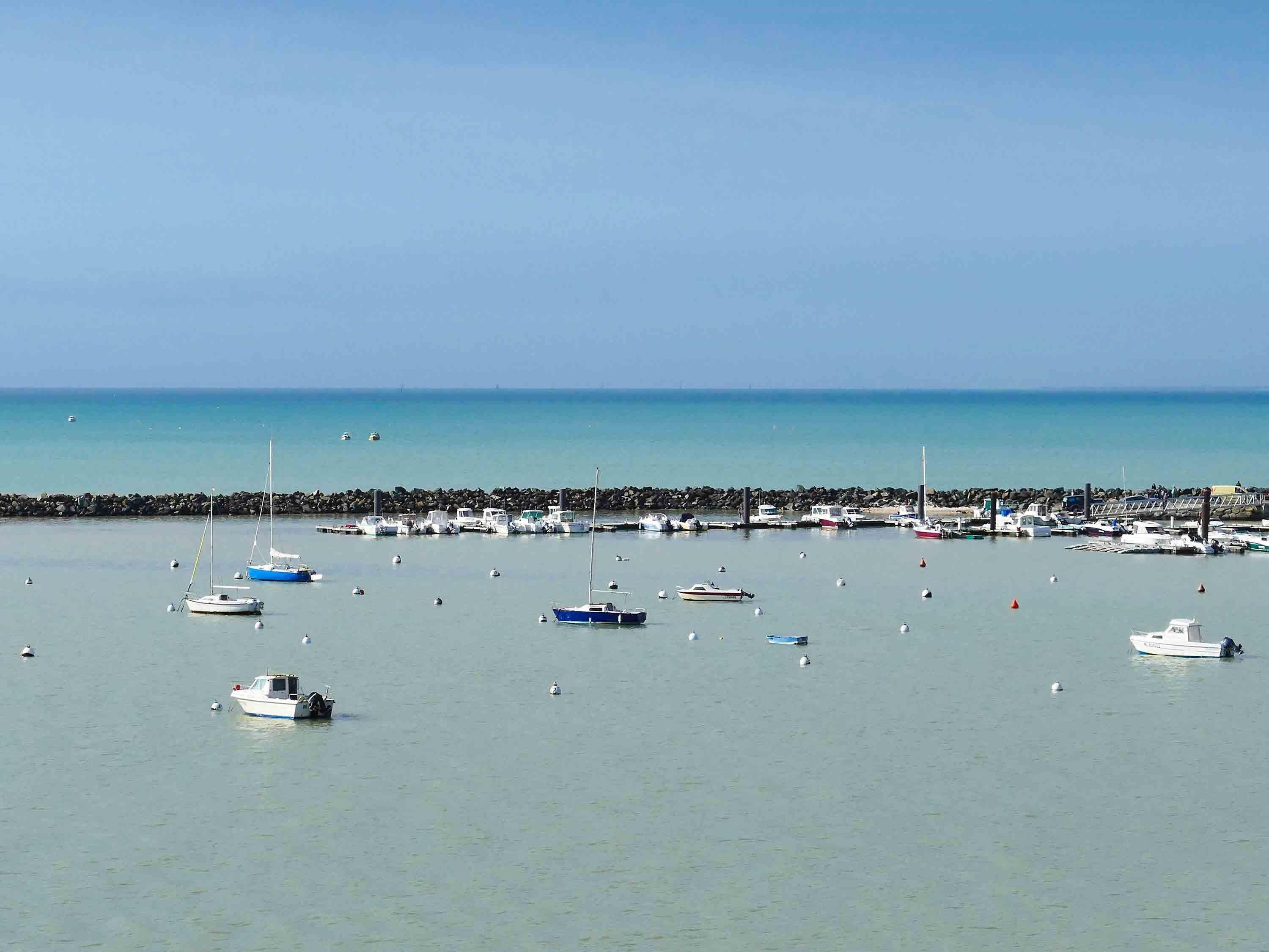 Un port esportiu amb diverses embarcacions amarrades, un moll de pedra i aigua tranquil·la.