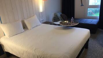 Ein Hotelzimmer mit einem großen Bett, einem kleinen runden Tisch mit einer Flasche, einem Stuhl und einem Fenster mit Blick nach draußen.