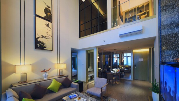 A spacious living area with a high ceiling, a dining area, and a kitchen visible through an open door. - Huafa Exhibition Executive Aparthotel (Zhuhai)