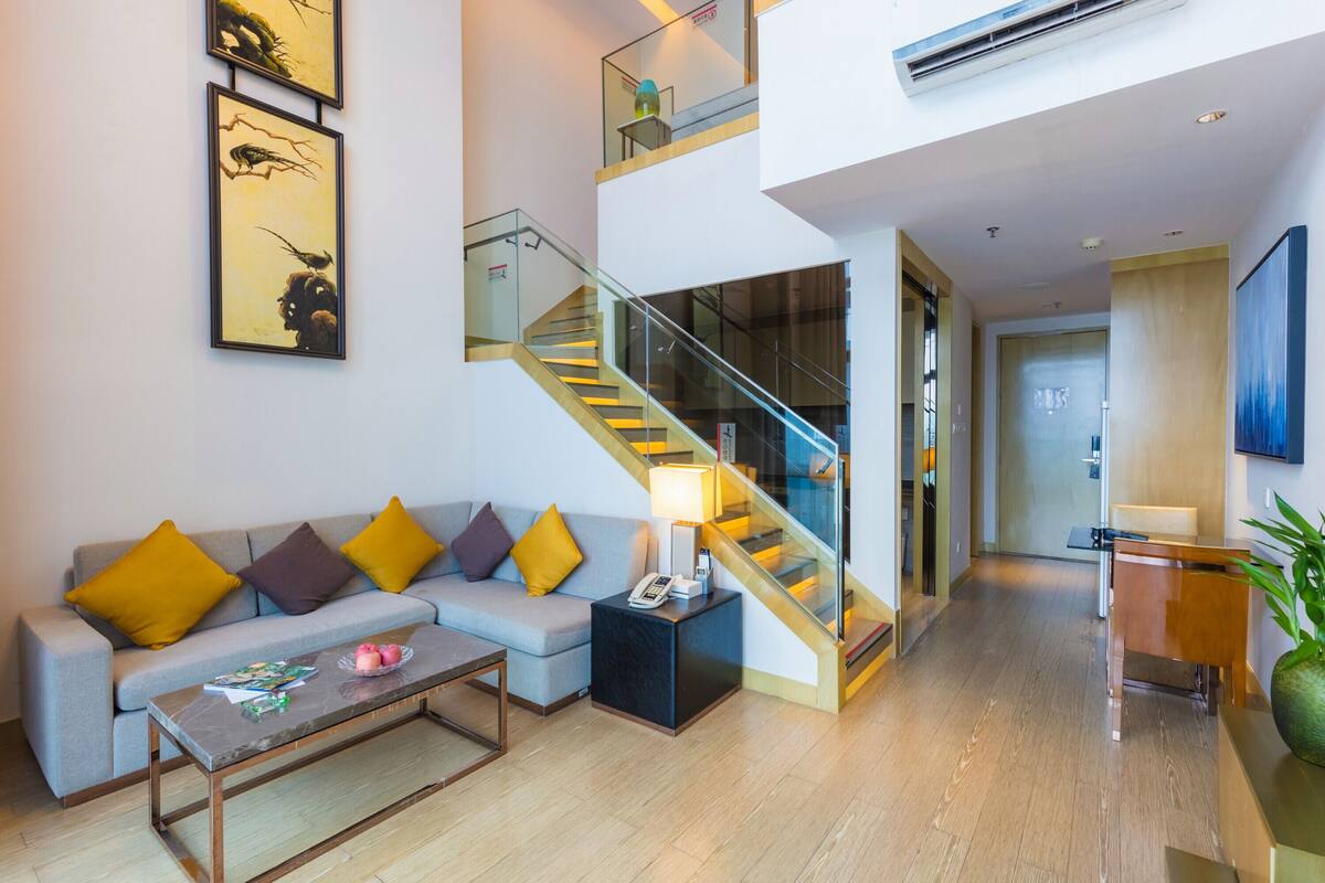 Una sala de estar moderna con un sofá gris, una mesa de centro y una escalera con barandas de cristal.