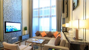 A modern living room with a sofa, armchairs, a coffee table, and a flat-screen TV mounted on a textured wall. - Huafa Exhibition Executive Aparthotel (Zhuhai)