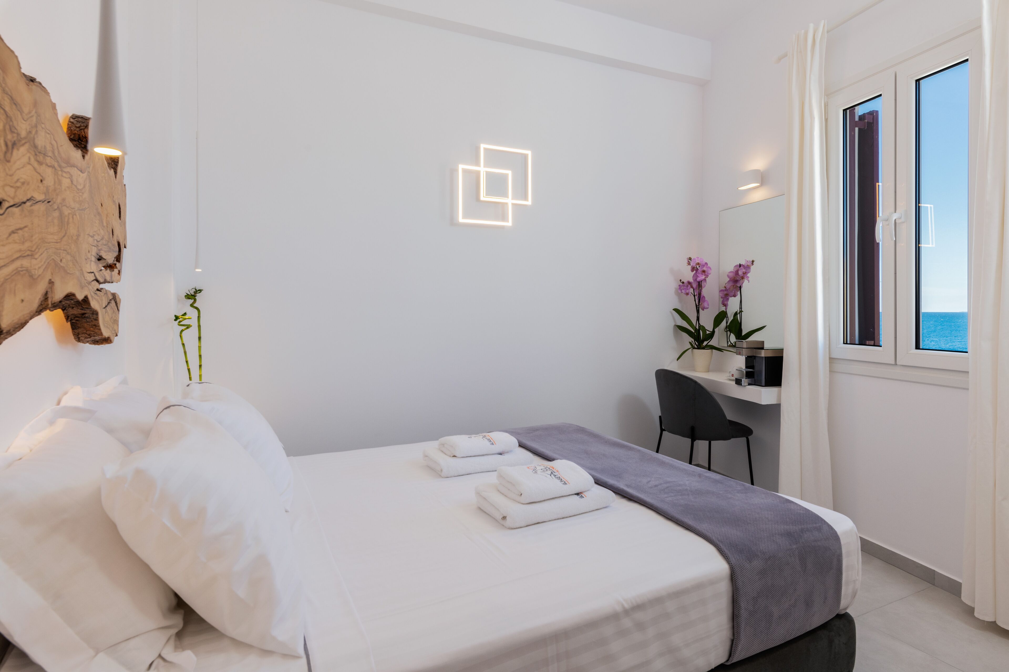 Un dormitorio moderno con una cama grande, un escritorio y vistas al mar a través de una ventana.