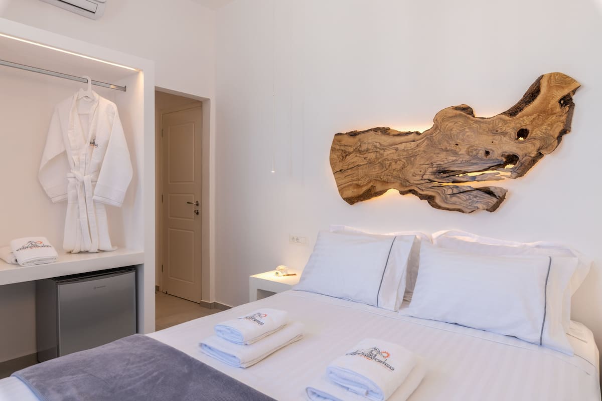 A hotel room with a bed, a bedside table, a nightstand, a towel rack, and a large piece of wood art on the wall.