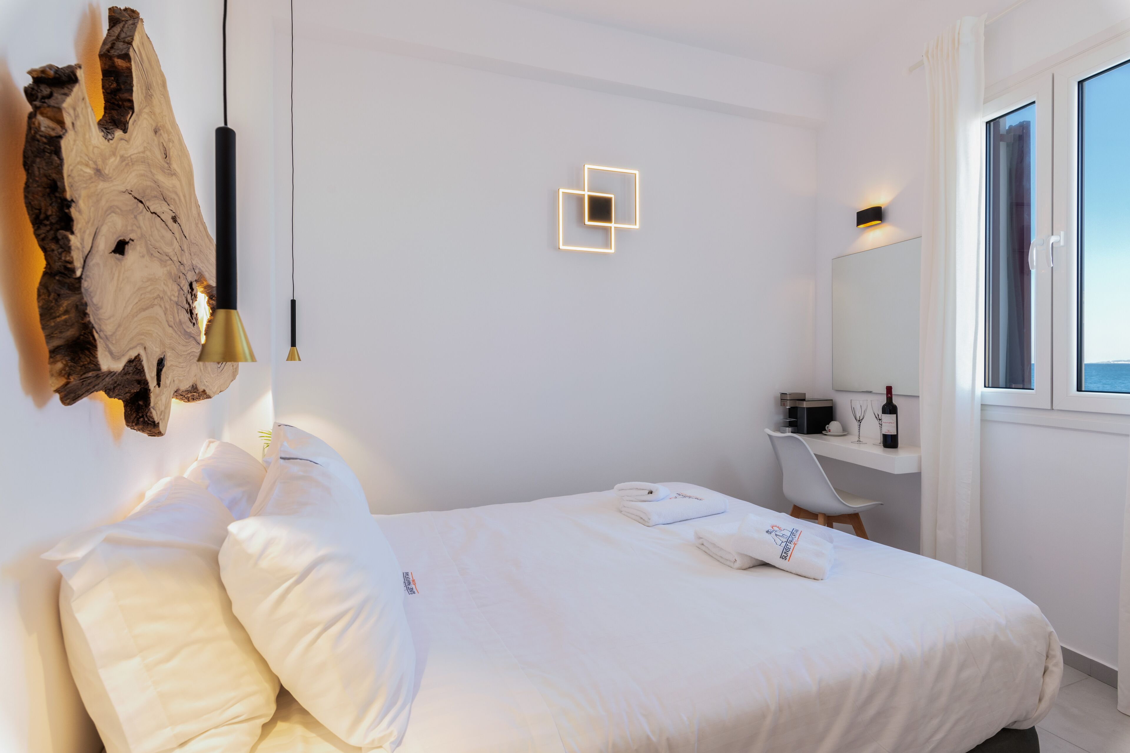 Una habitación de hotel con una cama, un tapiz de piel, una lámpara colgante, una mesita de noche con una botella y una ventana con vistas.