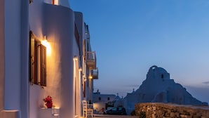 A white building with a balcony, a stone wall, and a mountain in the background. - Sunset Paraportiani Rooms (Mykonos)