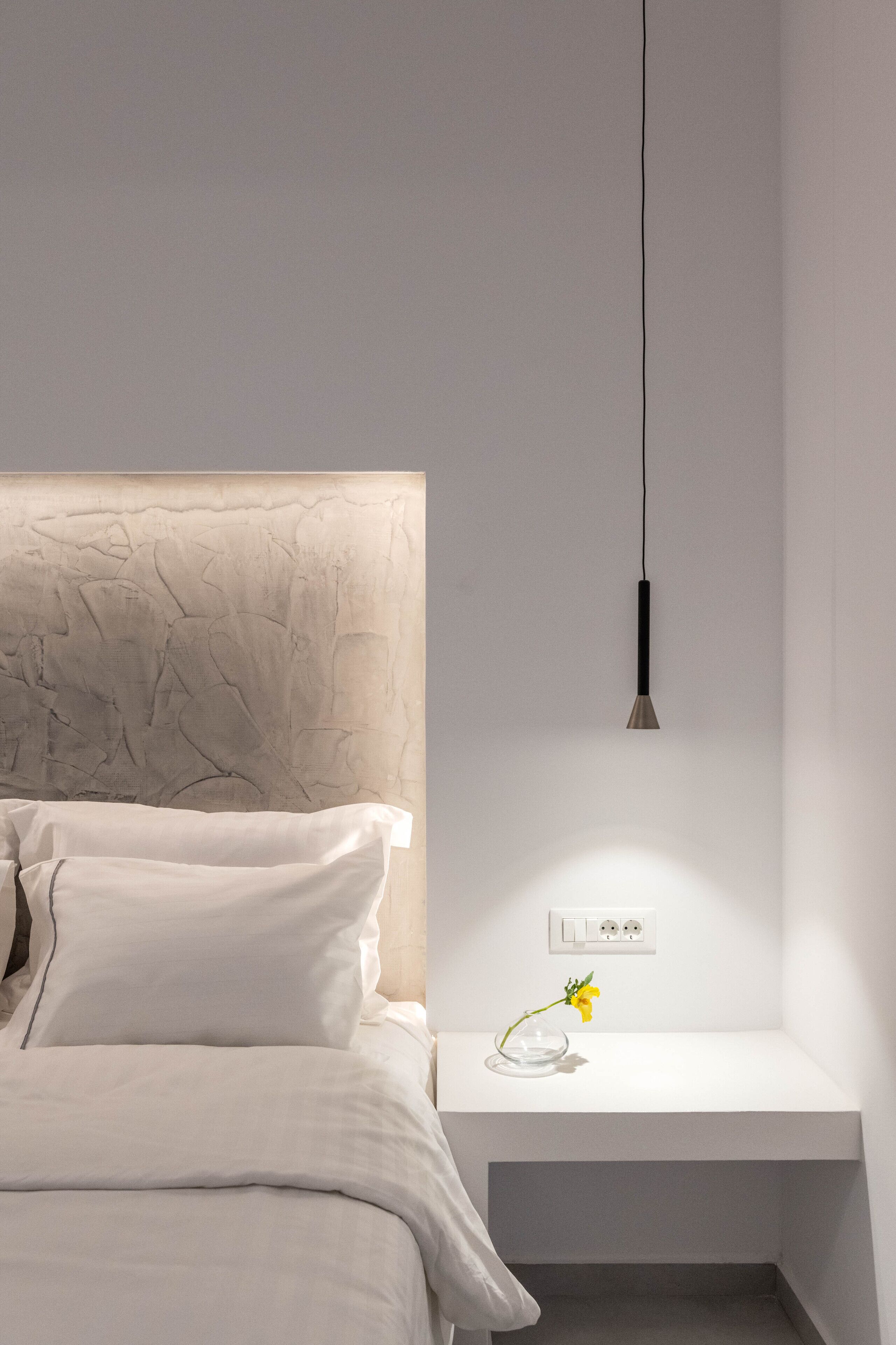 Un dormitorio minimalista con cama, mesita de noche y lámpara colgante.
