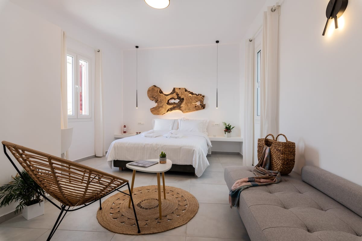 A modern bedroom with a bed, a chair, a sofa, and a wall-mounted light fixture.