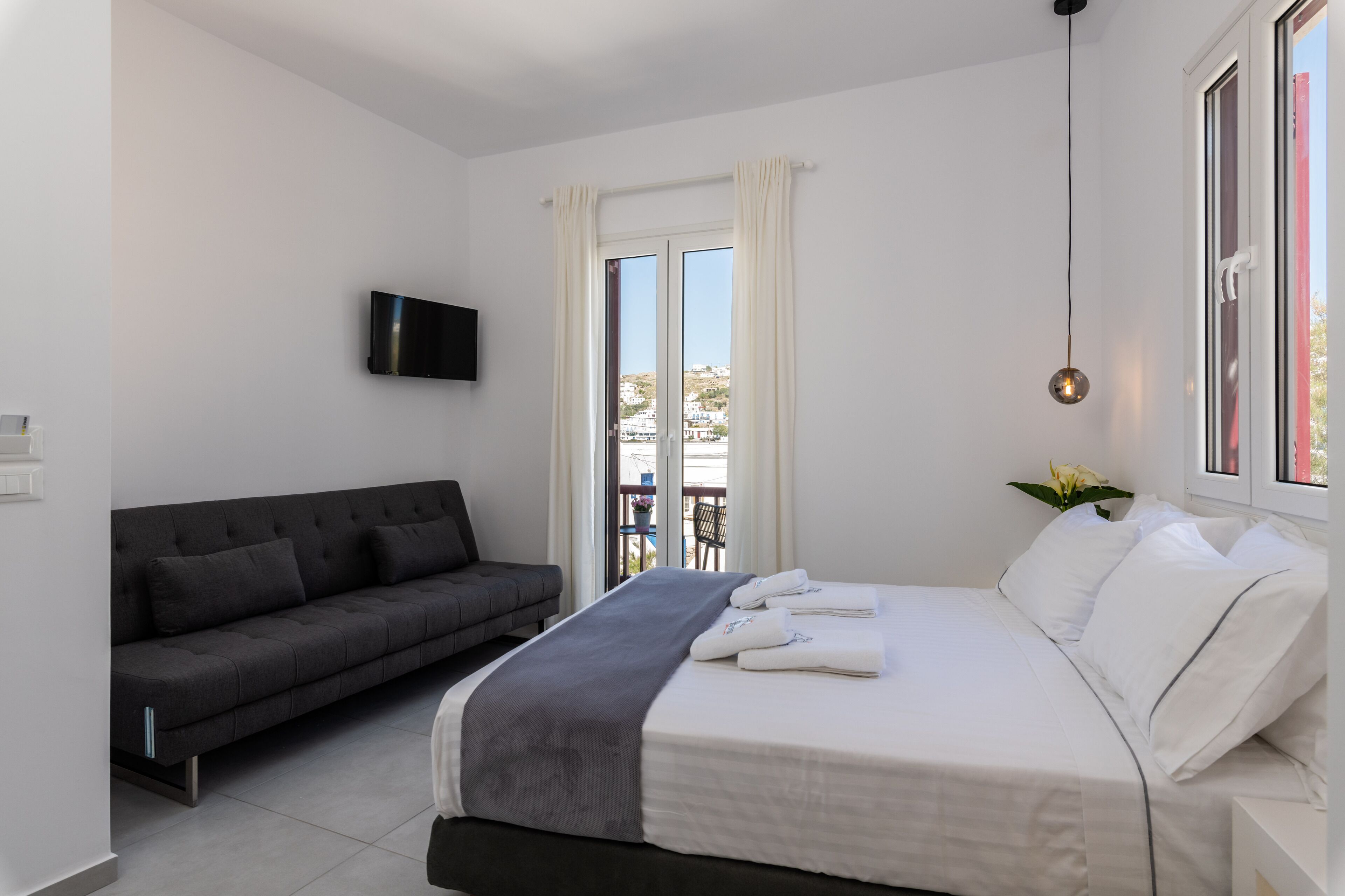 Una habitación de hotel moderna con cama, sofá, televisión y balcón con vistas.