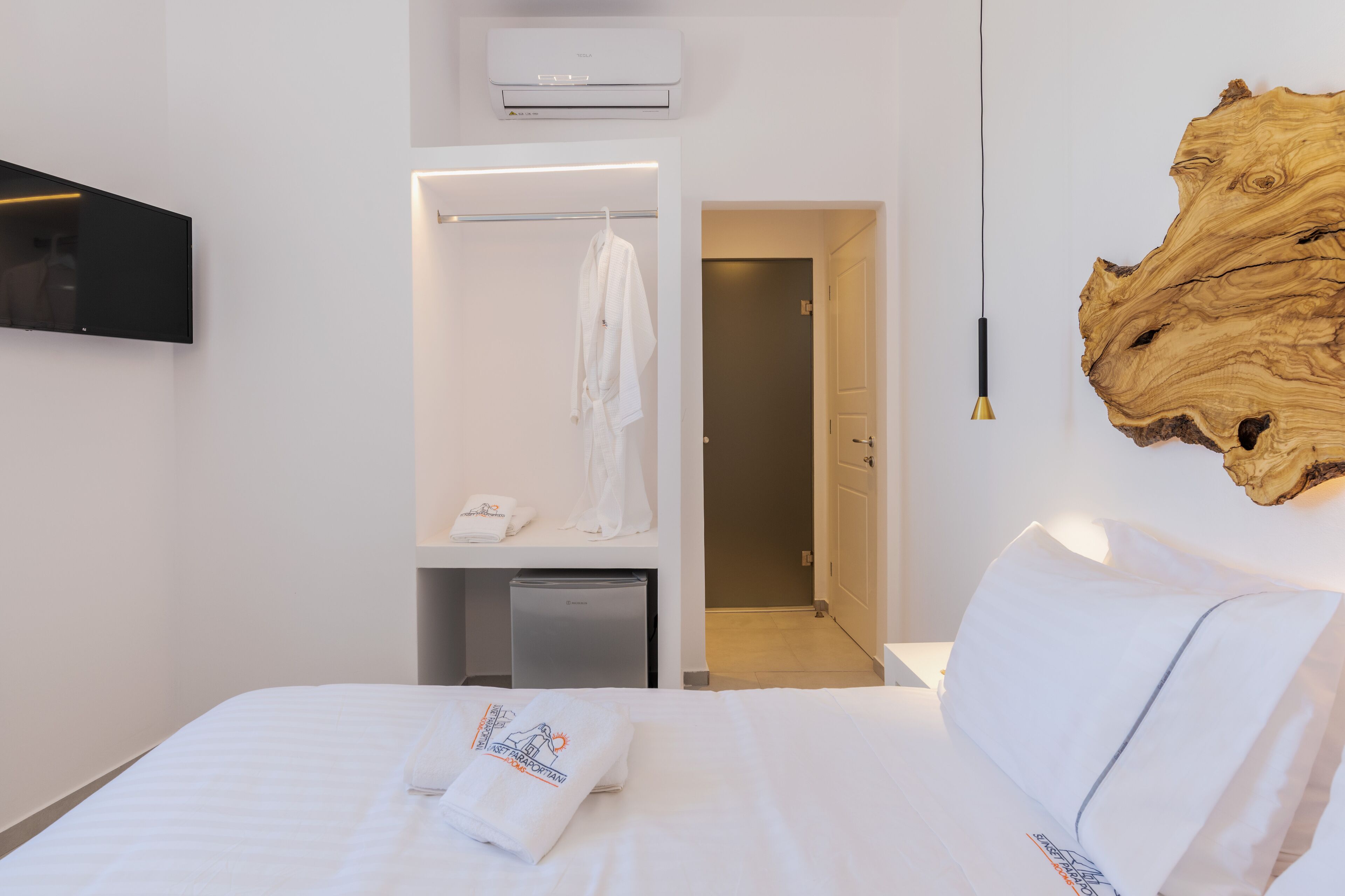 A hotel room with a bed, a wardrobe, a desk, a television, and a large wooden artwork on the wall.