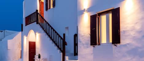 A white building with a staircase, a door, and a window with shutters.