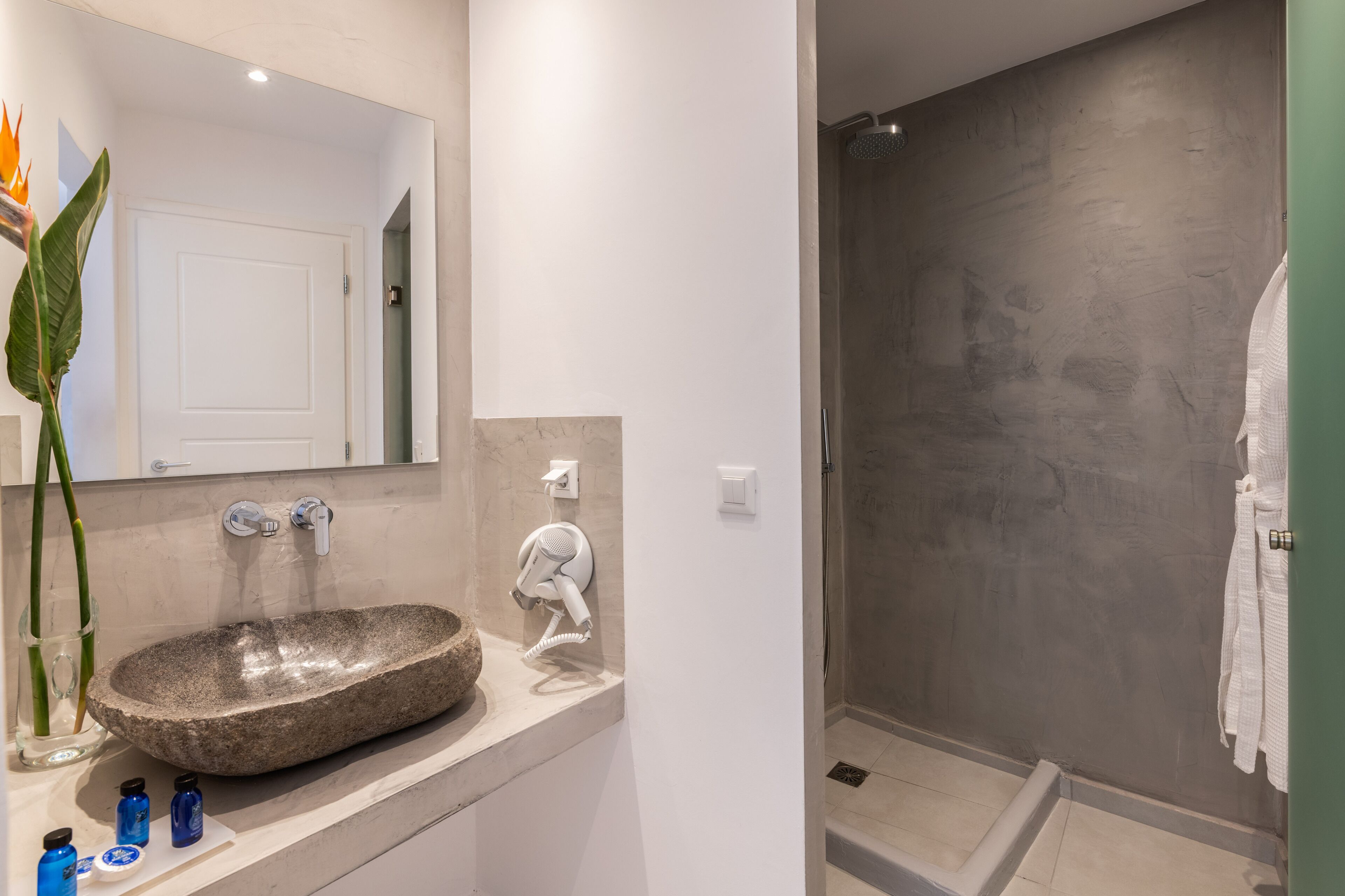 Une salle de bain moderne avec un lavabo en pierre, un sèche-cheveux et une cabine de douche en verre.