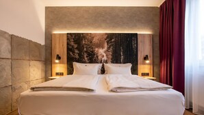 Una habitación de hotel moderna con una cama grande, dos lámparas de noche y un mural temático de bosque.