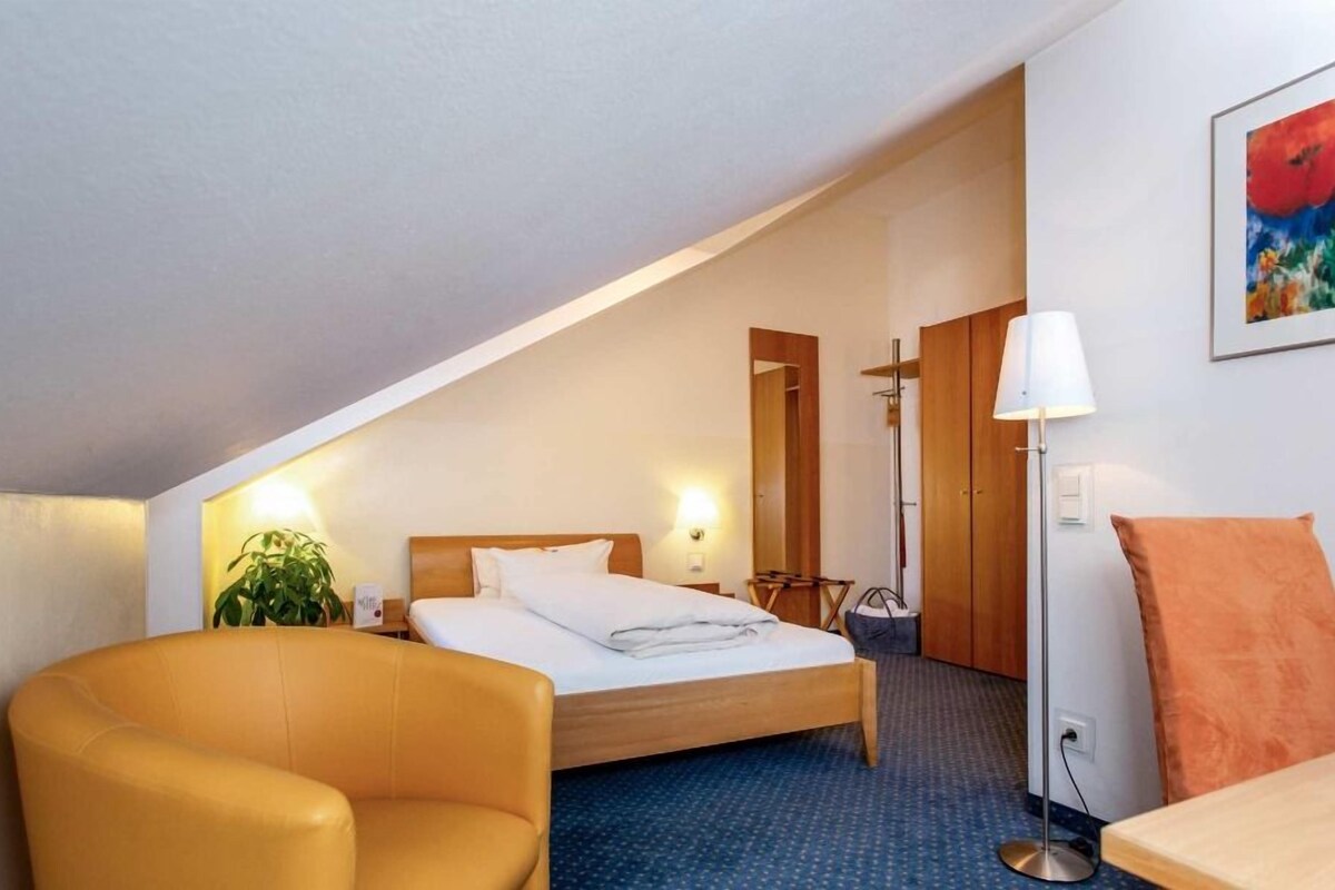 Een hotelkamer met een bed, een bureau, een stoel, een lamp en een schilderij aan de muur.