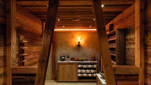 Un interior de madera con una barra central, estantes con botellas y una lámpara fijada a la pared.