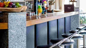 Una zona de bar con mostrador de madera, varios taburetes, lámparas colgantes y estanterías llenas de botellas.