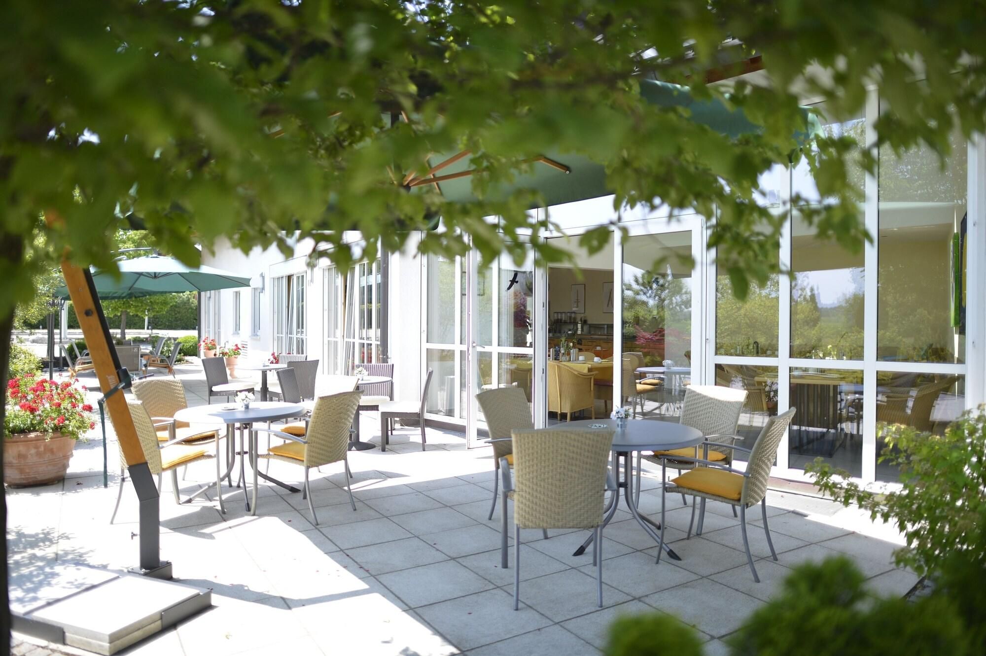 Ein Terrassenbereich im Freien mit Tischen, Stühlen, großen Fenstern und Blumentöpfen.