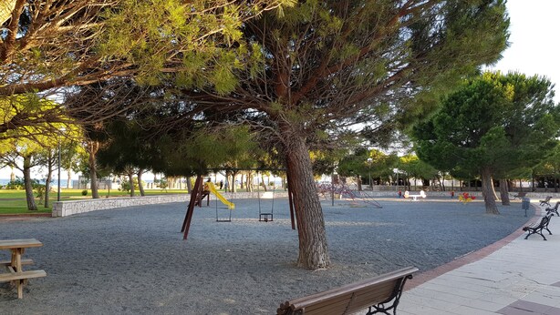 Ein Park mit einem Spielplatz, Bänken und einem großen Baum.